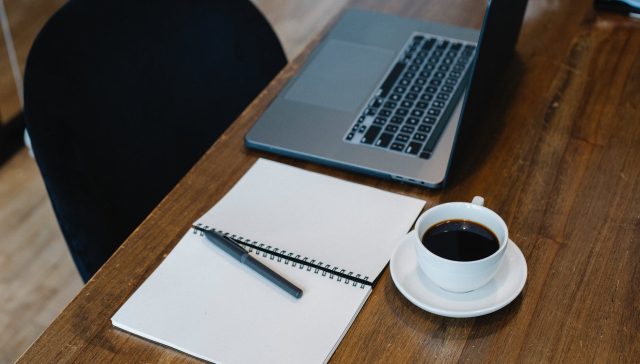 workplace with laptop and notepad placed near coffee cup