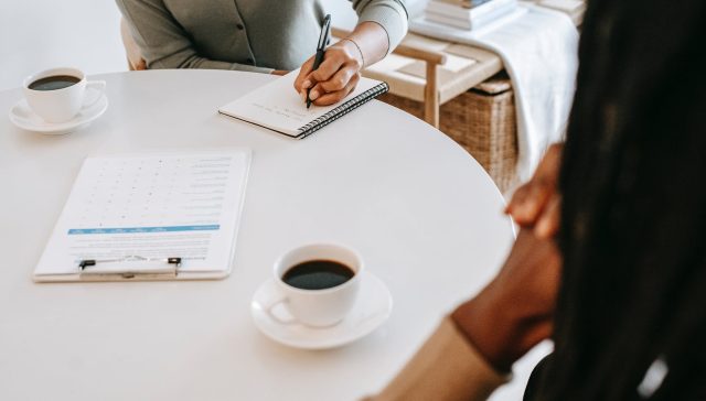 crop interviewer writing in notepad and talking to job seeker