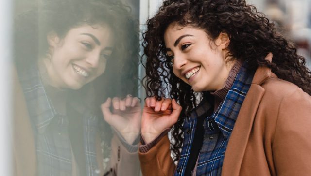 smiling woman with curly hair reflecting in street showcase