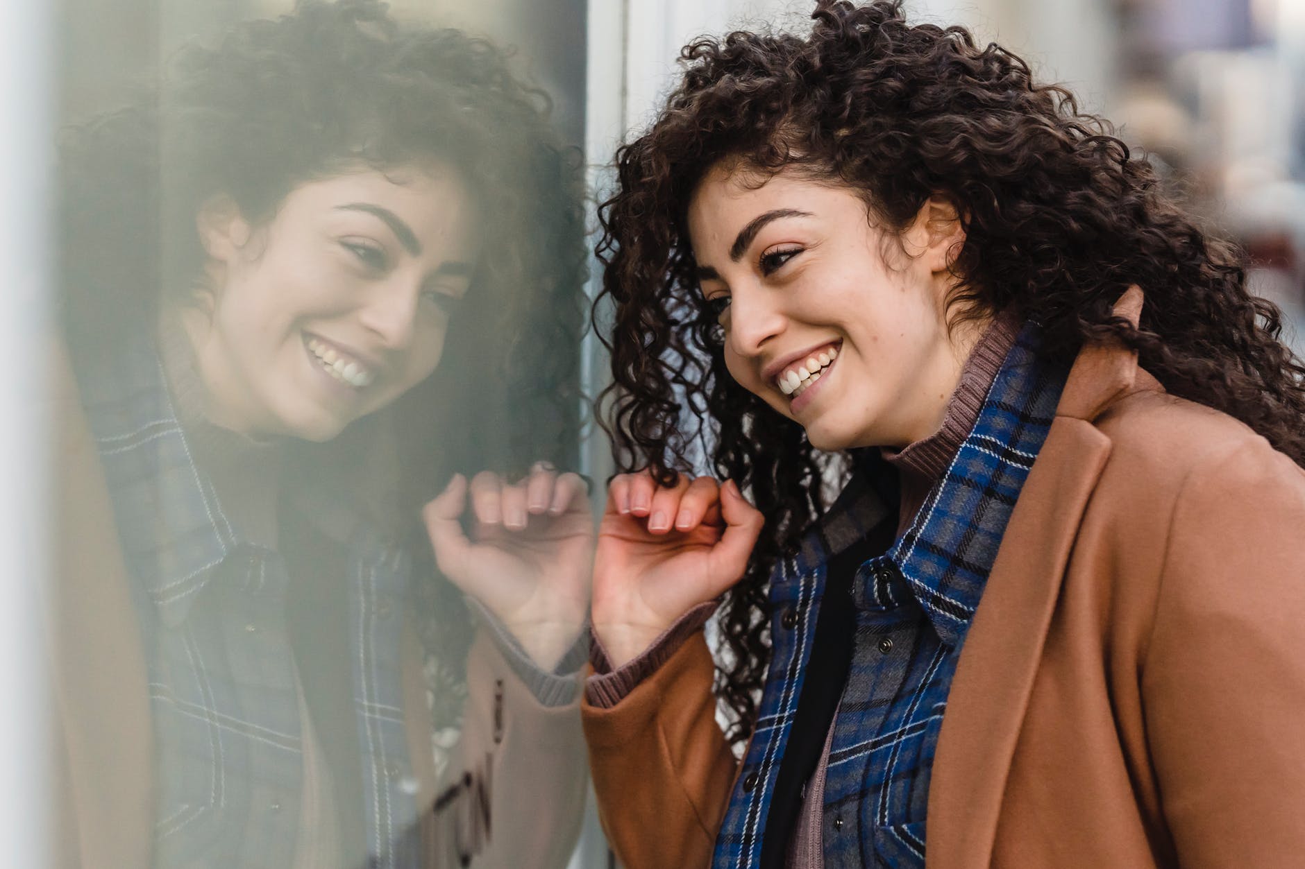 smiling woman with curly hair reflecting in street showcase