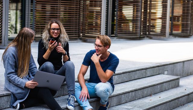 three persons sitting on the stairs talking with each other