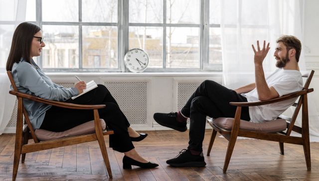 person in black pants and black shoes sitting on brown wooden chair